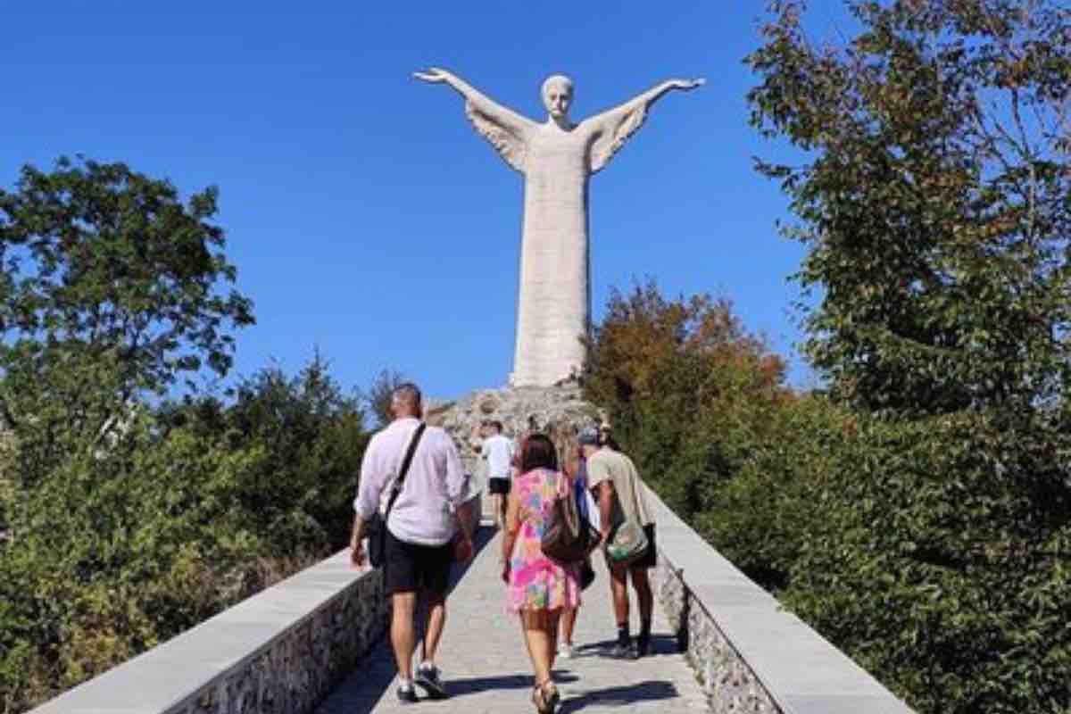 La testa di Cristo, con capelli corti e una barba appena accennata, è una rappresentazione diversa rispetto alla tradizione. Il gesto delle braccia aperte, con il braccio destro più sollevato, richiama un movimento di preghiera che non solo guarda verso la città, ma anche verso il mare, come se il Cristo volesse abbracciare tutto ciò che lo circonda.