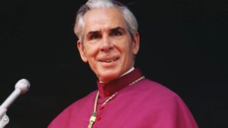 Mons. Fulton Sheen in abito vescovile davanti a un microfono