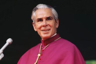 Mons. Fulton Sheen in abito vescovile davanti a un microfono