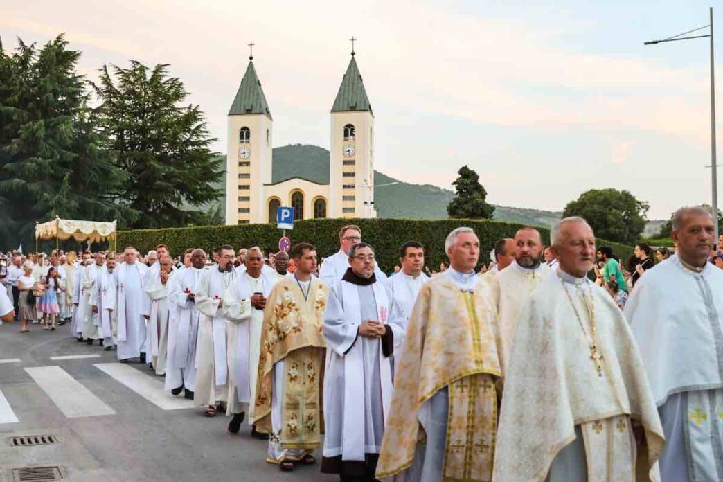 Processione eucaristica del Corpus Domini con ostensorio portato dal sacerdote sotto baldacchino tra fedeli in una via del paese