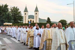 Processione eucaristica del Corpus Domini con ostensorio portato dal sacerdote sotto baldacchino tra fedeli in una via del paese