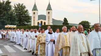 Processione eucaristica del Corpus Domini con ostensorio portato dal sacerdote sotto baldacchino tra fedeli in una via del paese